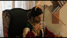 a woman is sitting in a chair drinking from a cup with a bookshelf in the background