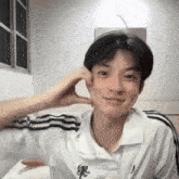 a young man wearing a white shirt with black stripes on the sleeves is smiling