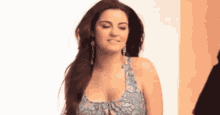 a woman with long hair is wearing a blue dress and earrings and is making a funny face .