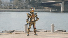 a man in a black and gold costume with the letter x on his chest is standing in front of a body of water
