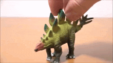a person is playing with a toy dinosaur on a wooden table .