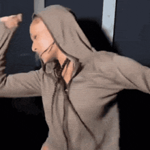 a woman wearing a hoodie and a headset is dancing with her arms outstretched