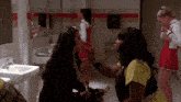 a woman applying makeup to another woman in a bathroom with cheerleaders in the background