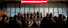 a group of people are standing in front of a large american flag