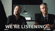 two men are sitting next to each other in a room and talking .