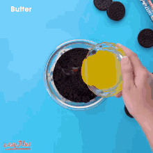 a person is mixing oreos in a glass bowl on a blue surface