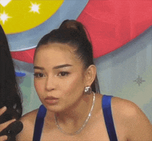 a woman with a ponytail and a necklace is talking into a microphone .