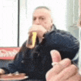 a man is sitting at a table drinking a beer and giving a thumbs up sign .