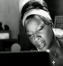 a woman wearing a headband and a cross necklace is looking at a computer screen