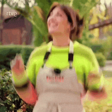 a woman wearing overalls and a neon green sweater is dancing in front of a sign that says rtve .