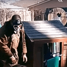 a man wearing a mask and goggles is standing next to a dog house .