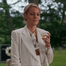 a woman in a white striped suit and tie holds a glass of wine