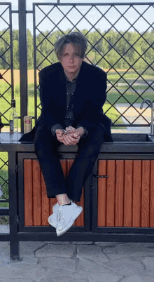 a man in a suit sits on a wooden cabinet next to a sink with a bottle of vodka on it