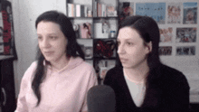 two women are sitting next to each other in front of a microphone and looking at the camera .