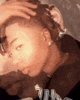 a close up of a person 's face with a hand on their head and earrings .