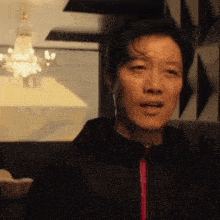 a man in a black jacket is making a funny face in a room with a chandelier in the background .