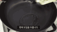 a person is cooking vegetables in a frying pan on a stove with korean writing on the bottom .