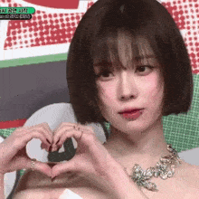 a woman with short hair is making a heart shape with her hands while wearing a necklace