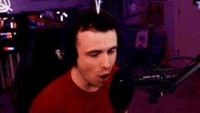 a man wearing headphones and a red shirt is standing in front of a microphone in a room .