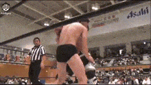 two men are wrestling in a ring with a referee and a sign that says asahi in the background .