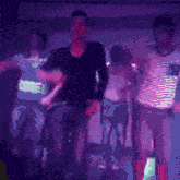 a group of people are dancing in a dark room with purple lights
