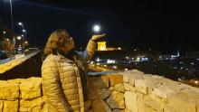 a woman stands on a stone wall looking up at the moon