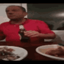 a man in a red shirt is sitting at a table holding a bottle of soda .