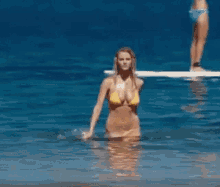a woman in a yellow bikini is standing on a beach .