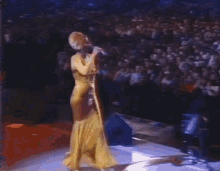 a woman in a yellow dress is singing into a microphone on a stage .