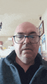 a bald man wearing glasses and a black shirt looks at the camera