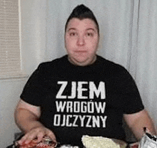 a man wearing a black shirt is sitting at a table eating food .