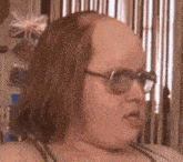 a woman with glasses and a bald head is wearing a wig .