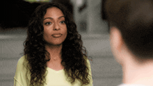 a woman with curly hair and a yellow shirt looks at a man