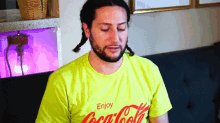 a man wearing a yellow coca cola shirt sitting on a couch