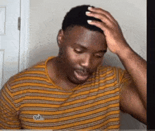 a man in a yellow striped shirt is holding his head .