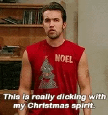 a man wearing a red shirt with a christmas tree on it is standing in front of a bookshelf .