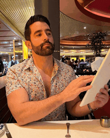 a man with a beard is sitting at a table reading a menu