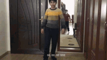 a boy in a striped sweater is standing in front of a door with the time 00 00 00 0000
