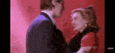 a man in a suit and a woman in a red dress are dancing together in front of a red background .