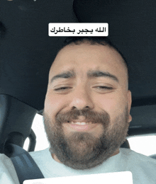 a man with a beard and mustache is smiling in a car with arabic writing on it