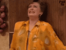 a woman in a yellow shirt is laughing in front of a wall of onions .