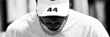 a black and white photo of a man wearing a white hat and a chain around his neck .