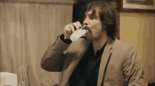 a man in a suit and mustache is drinking from a glass .