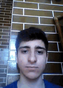 a young man is standing in front of a brick wall and looking at the camera