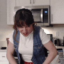 a woman in a denim vest is standing in front of a microwave that says ' on ' on it