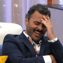 a man in a suit and tie is covering his face with his hand while smiling .