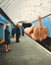 people waiting at a subway station with a giant hand giving a middle finger