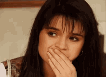 a woman is covering her mouth with her hand while looking at the camera .