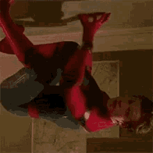 a man in a spiderman costume is hanging upside down from a ceiling .