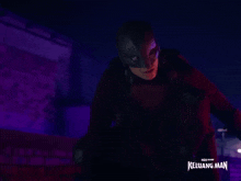 a man in a mask stands in front of a sign that says keluarg man